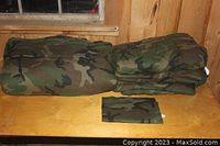 Two folded camouflage twin comforters and one folded camouflage pillowcase on wooden surface against wood panel background.