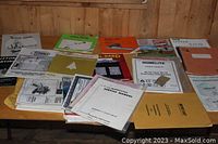 Multiple farm manuals and equipment instruction booklets laid out on a wooden table, some with visible writing and covers showing brand and equipment type.