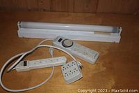 Photo showing white fluorescent light fixture along with three power bars on wooden surface.