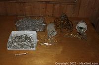 Overview of the lot on a wooden table showing a plastic container with glass balls, a white box with elongated prism parts, a cloth pouch with more prisms, a gold-toned metal light fixture base, and loose prisms and balls.