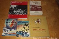 Five books arranged showing cover titles and illustrations on a wooden surface