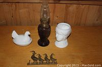 Complete lot overview showing all four items on wooden surface: milk glass lady cup, milk glass chicken dish, vintage lantern, brass duck hooks