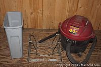 Shop Vac, garbage can, and metal stand setup on wooden floor against wood wall.