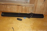 LG sound bar and remote displayed on wooden surface. Sound bar length shown by measuring tape near remote.