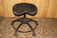 Front angled view of the black low stool showing contoured seat, metal legs, circular footrest, and caster wheels.