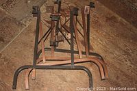 Two sets of metal folding table legs stacked together on the floor, visible rust and wear on metal surfaces, showing the frame and support braces.