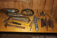 Various large hand tools on a wooden shelf showing hammers, fish tape reels, files, and chisels