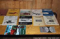 Top view of 12 assorted tractor and farm equipment manuals on a wooden surface, showing various brands and models.