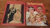Two vintage 1937 magazines side-by-side on a wooden surface. Left magazine titled The Illustrated London News featuring King George VI and Queen Elizabeth on the cover. Right magazine titled The Royal Family Coronation Yearbook with portraits of King George VI, Queen Elizabeth, and young royals on the cover.