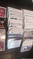 Image showing multiple stacks of hockey trading cards arranged on a black surface. Cards face down and some face up at the edges, showing white borders and colorful player images.