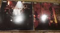 Both ABBA album covers; Super Trouper with group in spotlight, The Visitors with group in a dim room.