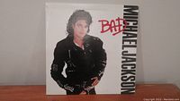 Front cover of Michael Jackson Bad vinyl record album with the artist in black leather jacket on white background and red/black text.