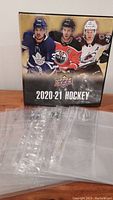 Front view of Upper Deck 2020-21 hockey card binder displayed vertically behind thirteen clear nine-pocket card pages spread out in front.