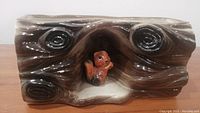 Front view of brown ceramic planter shaped like a log with a hollow containing a squirrel figurine