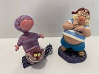 Cheshire Cat and Mr Smee sculptures displayed together showing size difference and detail.