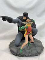 Front view of cold-cast porcelain statue of Batman and Robin with Batman kneeling and pointing, Robin aiming a slingshot
