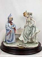 Front view of porcelain sculpture showing Cinderella and Fairy Godmother on oval wood base with brass name plaque.