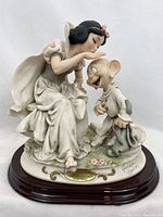 Front three-quarter view of porcelain Snow White and Dopey figurine on wooden base with plaque