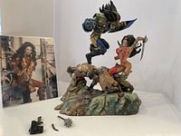 Photo showing the main statue with two crouching attackers, the female character with mace, blue and yellow armored male figure, broken parts positioned nearby, and autographed photograph.