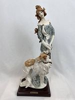 Front view of porcelain figurine featuring a woman in blue floral dress with curly brown hair standing next to a Borzoi dog, on wooden base with plaque.