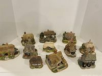 Group view of 10 Lilliput Lane miniature cottages featuring various thatched and tiled roof designs, stone and brick facades, and detailed landscaping.
