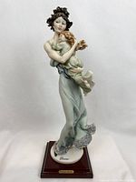 Front view of the mother's love figurine showing mother holding child in flowing green dress on wooden base.