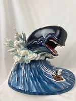 Front view of porcelain sculpture showing Monstro emerging from wave with raised foam and raft with Geppetto and Pinocchio
