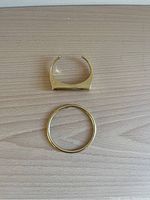 Top view of two gold-coloured brass bracelets: a rectangular-topped cuff and a circular bangle on a wooden surface.