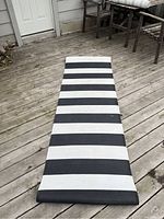 Full view of the black and white striped patio rug runner laid out on a wooden deck showing its length and color pattern.