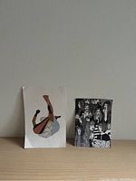 Photo showing two unframed prints side-by-side against a plain wall: left print is an abstract figure by Michelle Furlong with some discoloration; right print is a monochrome detailed drawing with multiple human faces by unknown artist.