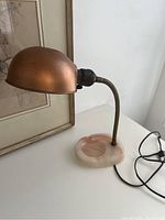 Overall view of the gooseneck brass lamp showing the dome-shaped shade and the pink acrylic ashtray base with swirling patterns.