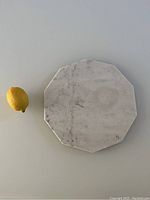 Top view of the octagonal white marble trivet on a light surface with a lemon for scale.