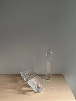 Two clear leaf-shaped glass bowls and a tall clear glass bird-shaped sculpture displayed on a wooden surface against a plain gray background.