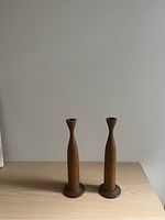 Photo of a pair of teak wood candle sticks with smooth, tapered shape and flared top along with round bases for holding taper candles.