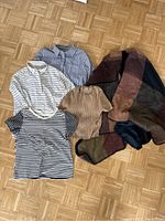 Top-down view of four clothing items laid flat: two striped dress shirts, one ribbed cropped t-shirt, and one check patterned cape.