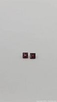 Pair of square cut natural garnet gemstones with a vibrant hot pink to vivid red color on a grey background.