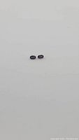 Pair of small oval cut deep purple sapphires on a plain white background, showing size and color.