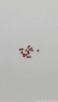 Cluster of bright cherry red garnet stones on a white background, showing round diamond cuts, varying slightly in size