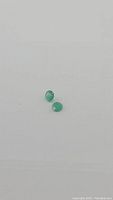 Two round-cut green emerald gemstones on white background