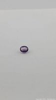 Oval cut deep purple amethyst gemstone laying on a white background, showing stone detail and color.