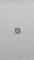 Close-up image of the square Ascher cut pink purple amethyst gemstone on a plain background.