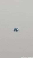 Front-facing photo of natural aquamarine gemstone on plain background showing the emerald cut and clarity