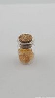 Small clear glass vial with cork stopper, filled with natural yellow-orange citrine crystals.