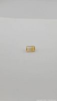 Close-up photo of a natural golden citrine, emerald cut gemstone on a white background to show shape and color.
