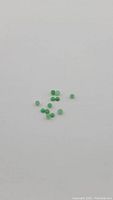 Close-up photo of several small round green jade cabochon cut gemstones spread out on a white surface, showing polished domed shape and green color.