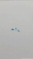 Photo of three natural paraiba blue apatite gemstones placed on a plain white background.