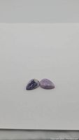 Two natural purple pear cabochon opal gemstones positioned side by side on a plain surface.