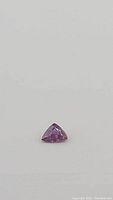 Front view of a pinkish purple trillion cut sapphire on white background showing color and cut details.