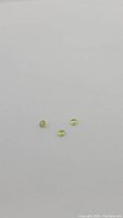 Photo of three small round cut sphene gemstones, light greenish-yellow, spaced on plain white background.