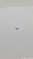 Overview photo showing two small oval cut, light bluish-purple natural tanzanite gemstones on plain white background, sized to compare.